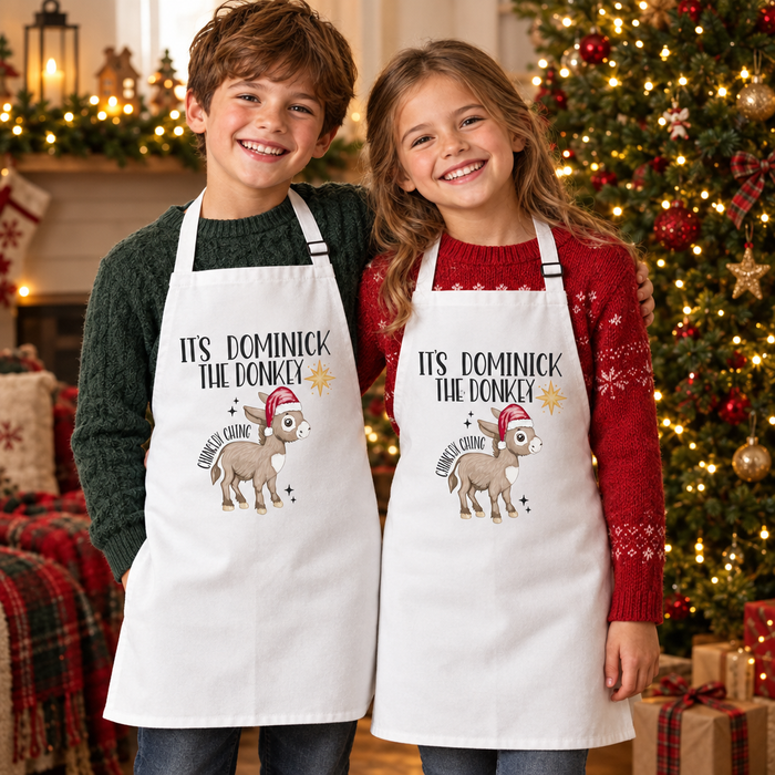 Boy and girl wearing Dominick the Donkey aprons beside a Christmas tree