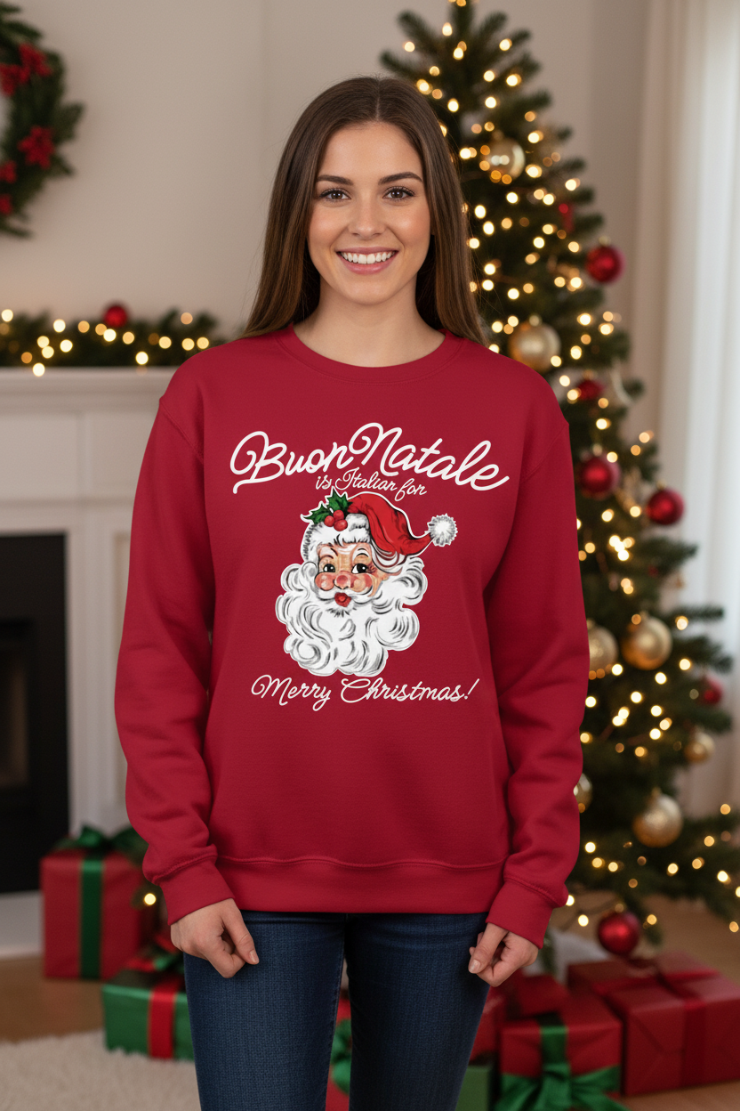 A woman wearing a red crewneck sweatshirt with a 'Buon Natale' Santa Claus graphic, standing in front of a decorated Christmas tree and fireplace.