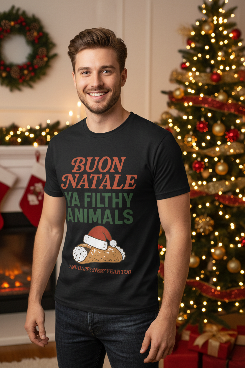 A man wearing a black graphic t-shirt with a Christmas-themed design in Italian ('BUON NATALE YA FILTHY ANIMALS'), standing in a cozy holiday living room with a lit Christmas tree and fireplace in the background.