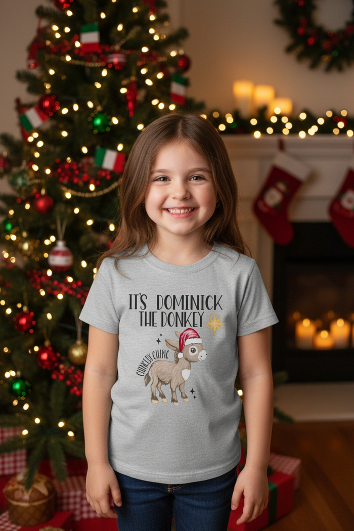 Five-year-old girl wearing the Dominick the Donkey shirt beside a Christmas tree