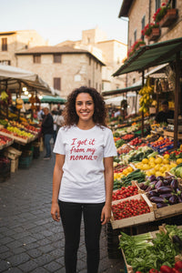 A white short-sleeve crewneck t-shirt featuring the phrase 'I got it from my nonna' printed in red cursive text across the chest, accompanied by a small red heart at the end.