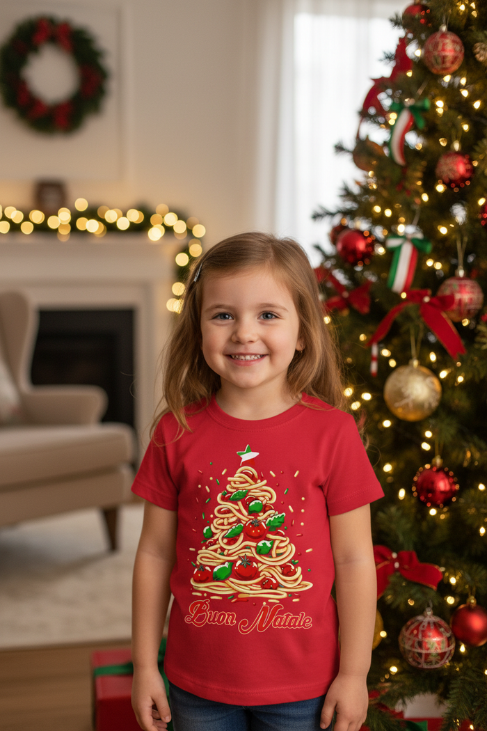 Little girl wearing the red Buon Natale Pasta shirt beside a Christmas tree