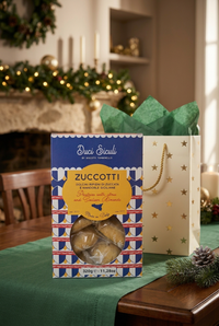 Zuccotti cookie box in a Christmas scene with a cream-and-gold gift bag and fireplace